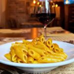 Piatto di pennette alla zucca con calice di vino rosso